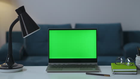working-table-in-home-office-with-laptop-lamp-book-and-glasses-green-screen-for-chroma-key-technology-zooming-shot-man-is-turning-off-table-lamp